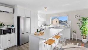 A modern kitchen with a central island, stainless steel appliances, and a view of a house through the window.