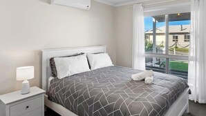 A hotel room with a bed, a nightstand, a lamp, and a window with a view.