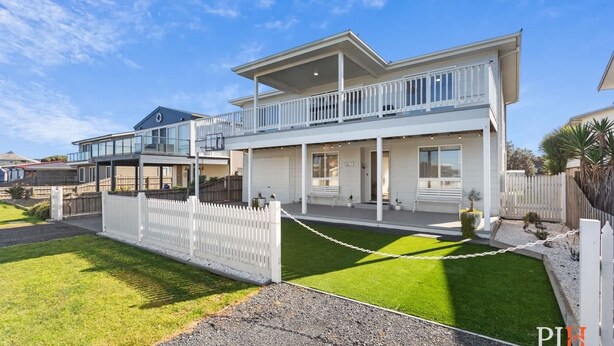 A two-story house with a covered porch, a garage, and a white picket fence.