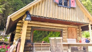 Une cabane rustique en rondins de bois, dotée d’un porche en bois, d’une grande fenêtre et d’un petit abri attenant.