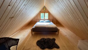 Une chambre confortable située sous les toits, avec un plafond en pente en bois, un lit avec des oreillers, un tapis en fourrure sur le sol et une fenêtre offrant une belle vue.