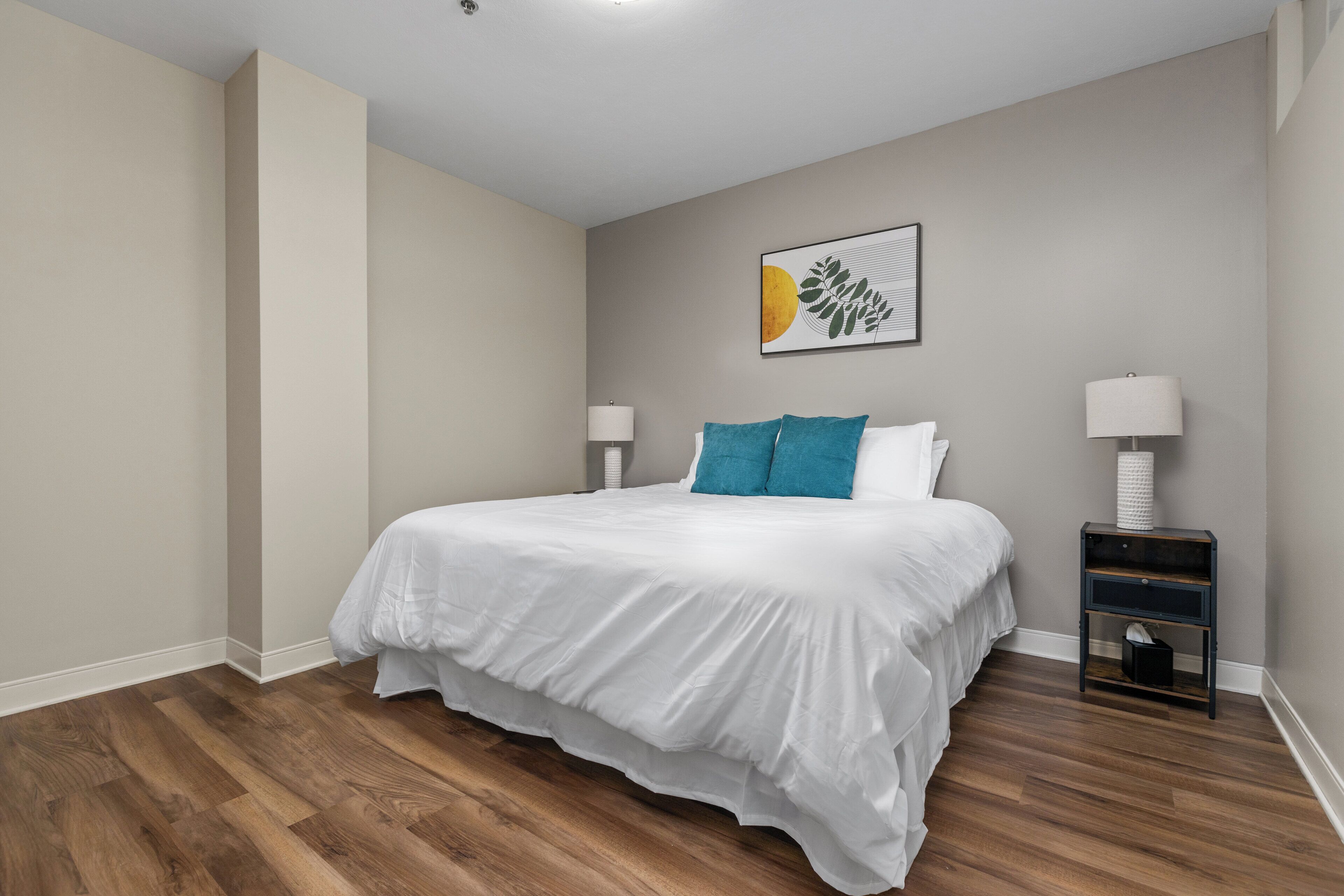 Une chambre à coucher avec un grand lit, deux tables de chevet et une œuvre d’art accrochée au mur.