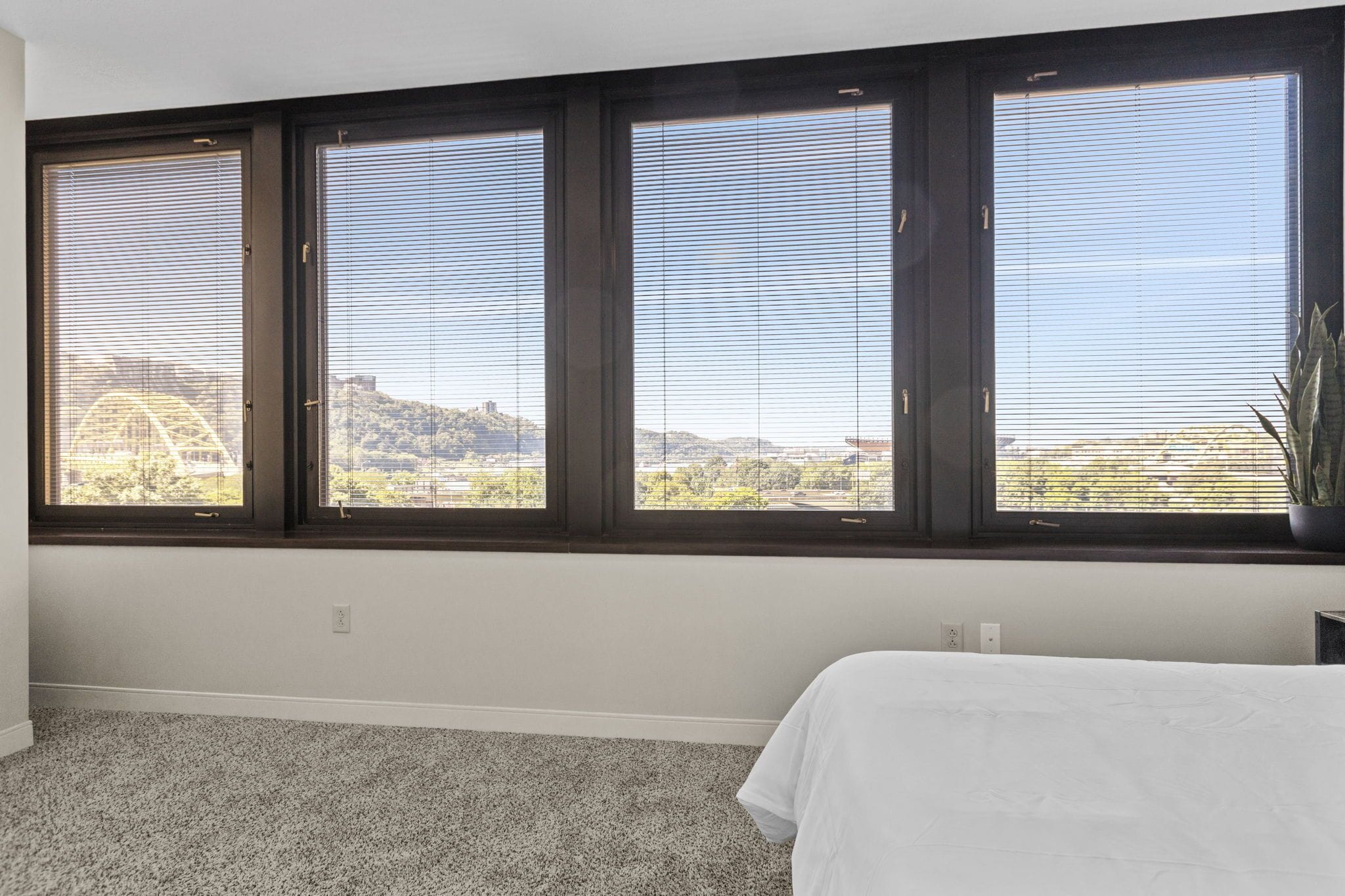A bedroom with a large window, carpeted floor, and a bed.