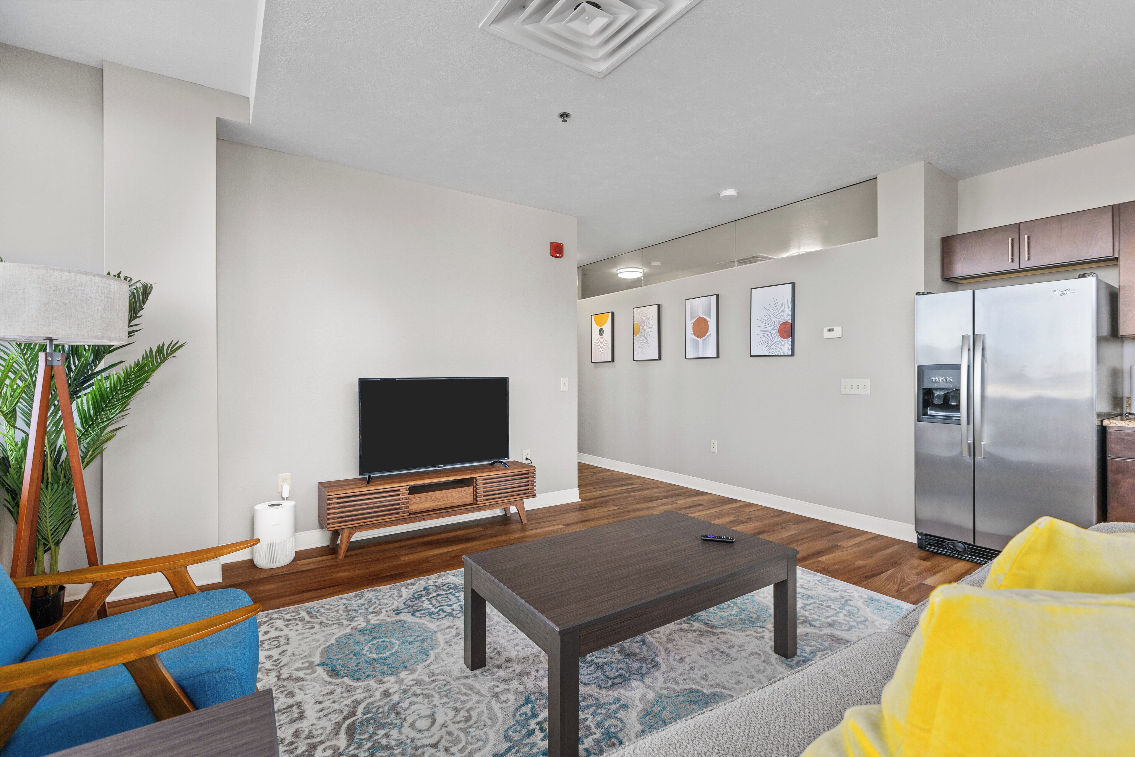 A modern living room with a flat-screen TV, wooden furniture, and a refrigerator.