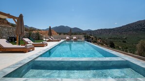 Une piscine rectangulaire à l’eau d’un bleu limpide, entourée de chaises longues en bois et de parasols.