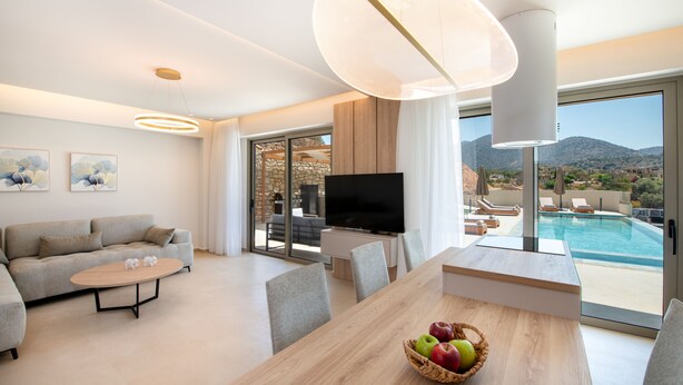 Un salon moderne avec un canapé, une table basse et une table à manger. On y trouve également un téléviseur, une grande fenêtre donnant sur la piscine et un luminaire au plafond.