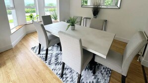 A modern dining room with a large table, six chairs, a potted plant, and a large mirror on the wall.