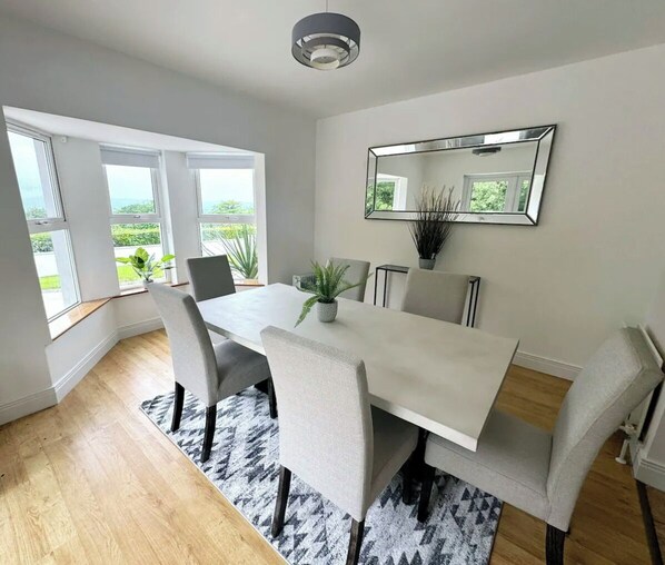 Un comedor moderno con una gran mesa, seis sillas, una planta en maceta y un espejo grande en la pared.