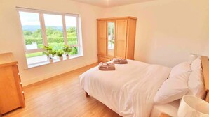 A bedroom with a large window, wooden wardrobe, and neatly made bed.