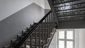 A staircase with ornate black balusters and a handrail, leading to a landing with a window. - RentPlanet - Apartament Świdnicka (Wroclaw)