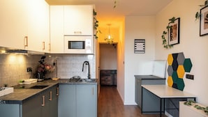 A modern kitchen with grey cabinets, a microwave, and a sink. There is a small dining area with a table and chairs. - RentPlanet - Apartament Świdnicka (Wroclaw)