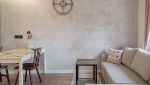 A living room with a round wall clock, a dining table with chairs, a sofa with cushions, and a small side table. - RentPlanet - Apartament Świdnicka (Wroclaw)