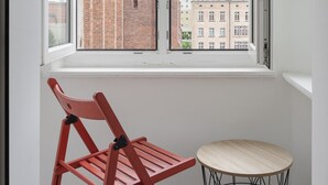 A room with a window overlooking a brick building and other buildings. There is a red chair and a small round table with a wireframe base. - RentPlanet - Apartament Świdnicka (Wroclaw)