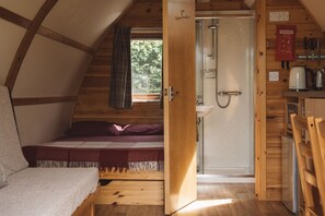 A compact room with a bed, a shower, and a small kitchenette. - Cosy En-suite Glamping Cabin with Hot Tub (Erwood)