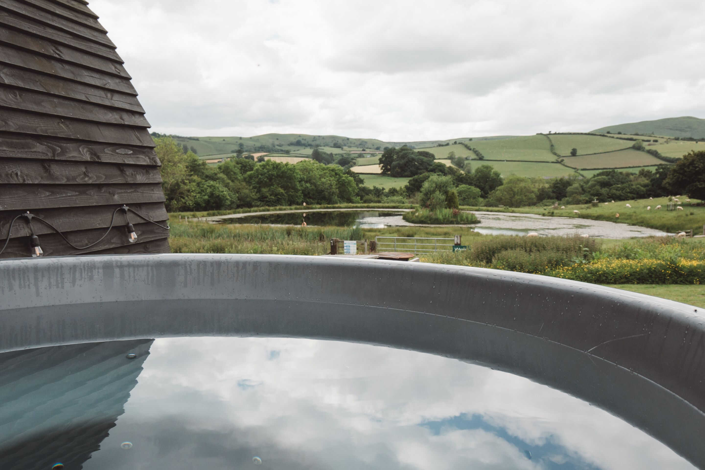 A hot tub with a view of rolling hills and a wooden building in the foreground.