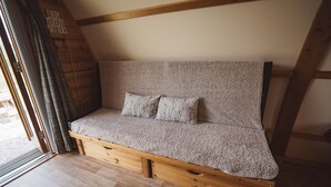 A cozy, wooden-framed sofa with a textured fabric, positioned in a room with wooden beams and a sloped ceiling. - Cosy En-suite Glamping Cabin with Hot Tub (Erwood)
