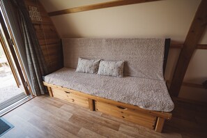 Un sofá acogedor de madera con estructura y tejido texturizado, ubicado en una habitación con vigas de madera y techo inclinado.