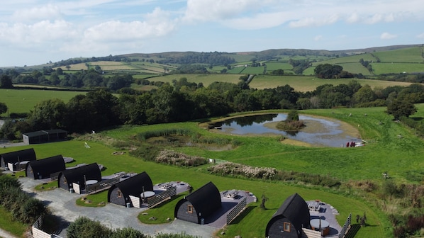 Un paisaje rural con un estanque, campos verdes y una hilera de casas de campo con techos negros.