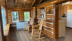 A log cabin interior with a dining area, kitchen, and a view of the outdoors.