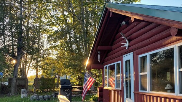 A wooden cabin with a deck, a flag, and a grill.