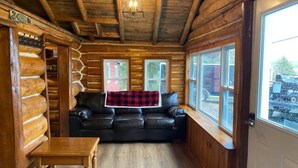 A log cabin interior with a leather sofa, a wooden table, and large windows.