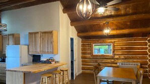 A rustic log cabin interior with a kitchen, dining area, and a large window.
