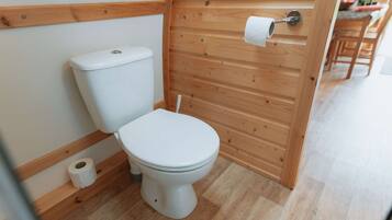 Un bagno piccolo con rivestimenti in legno, dotato di un water, uno scaffale di legno con un rotolo di carta igienica e una porta in legno.