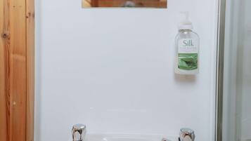 A bathroom with a white sink, a window, and a bottle of Silk hand soap.