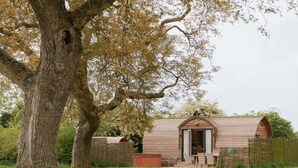 Eine rustikale Holz-Blockhütte mit geneigtem Dach, einer Holztür und einer kleinen Veranda mit Stuhl und Tisch.