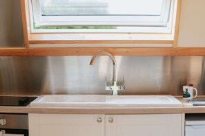 A kitchen with a stainless steel sink, wooden cabinets, and a window above the sink. - Cosy Rural Cabin With Hot Tub (Spalding)