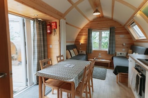 A cozy, wooden cabin with a dining area, a sofa, and a kitchenette. - Cosy Rural Cabin With Hot Tub (Spalding)