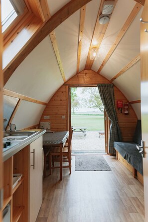 A cozy, wooden interior with a kitchen area, dining table, and seating. - Cosy Glamping Cabin With Wood Fired Hot Tub (Spalding)