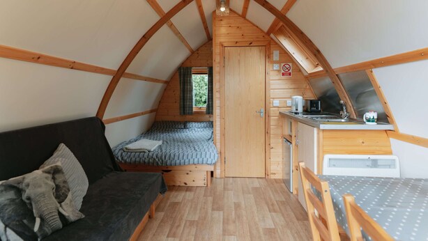 A compact, wooden interior with a loft bed, kitchenette, and a small seating area.
