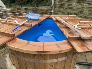 A wooden hot tub with a blue interior, surrounded by wooden benches and a rustic fence. - Cosy Glamping Cabin With Wood Fired Hot Tub (Spalding)