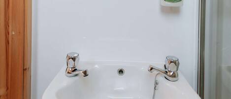Un baño con lavamanos blanco, ventana y una botella de jabón de manos Silk.