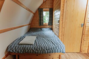 A small, wooden cabin room with a single bed, a window with curtains, and a wooden door. - Cosy Glamping Cabin With Wood Fired Hot Tub (Spalding)