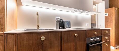A modern kitchen with wooden cabinets, a stainless steel sink, a coffee machine, and an oven.