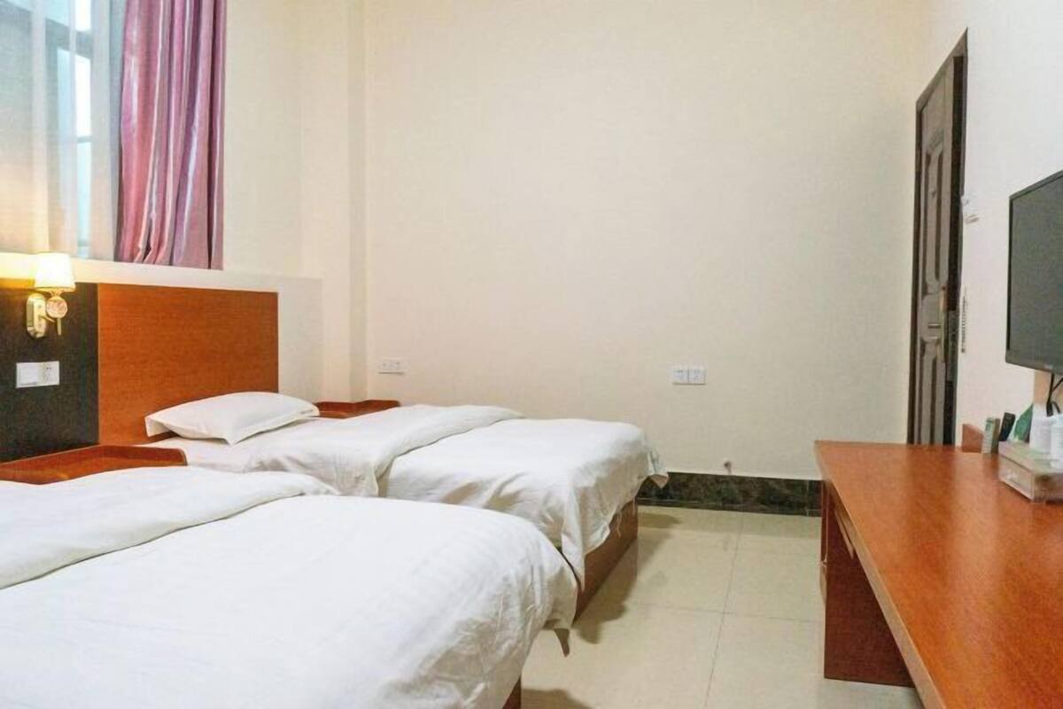 A hotel room with two single beds, a wooden headboard, a desk with a television, and a window with curtains.