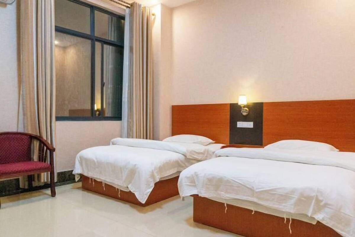 A hotel room with two single beds, a wooden headboard, a nightstand, a chair, and a window with curtains.