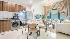 Uma cozinha moderna com eletrodomésticos embutidos, um espaço de refeições com uma mesa redonda e cadeiras, e uma sala de estar com um sofá e uma mesa de centro.
