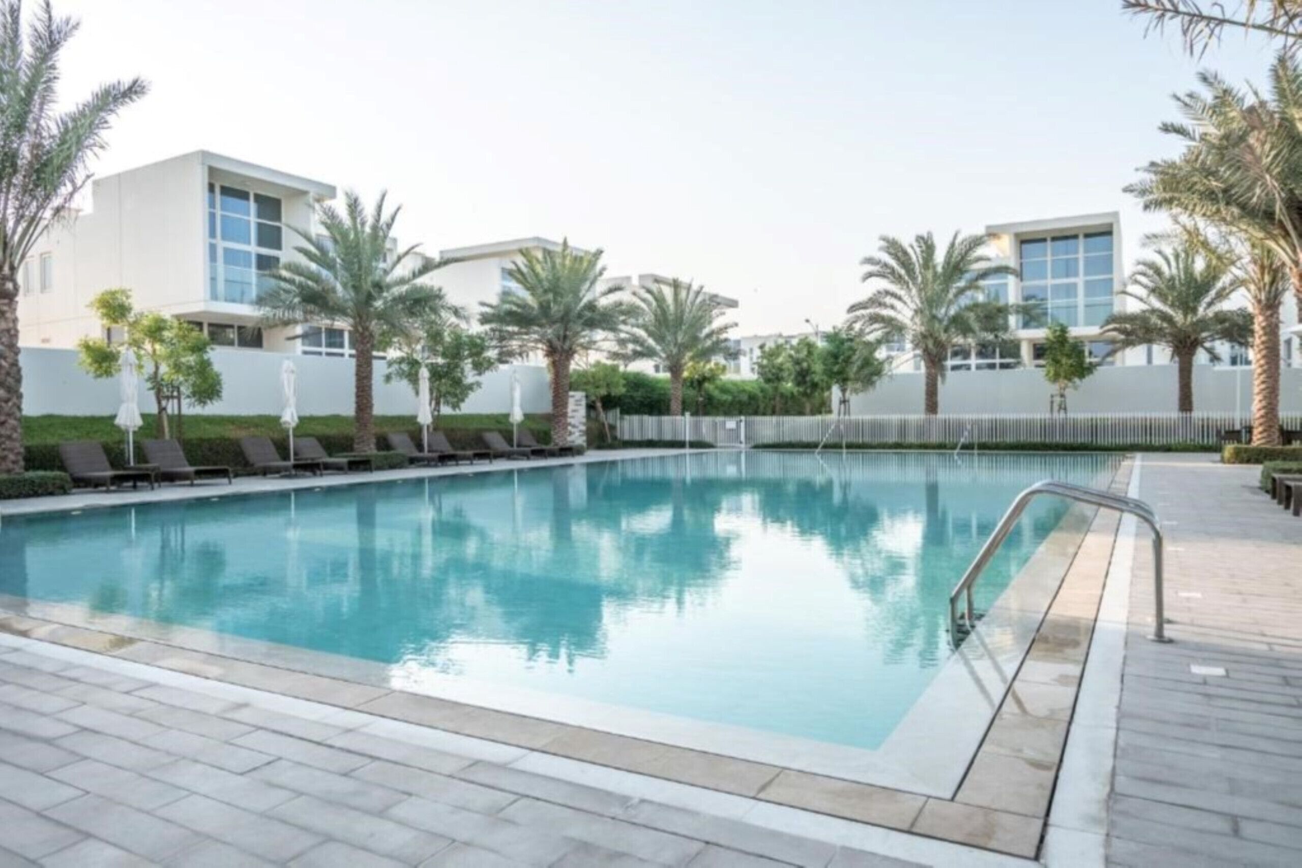 Ein Pool mit Liegestühlen und Palmen, umgeben von modernen Gebäuden.