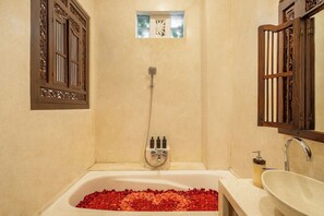 A bathroom with a bathtub filled with rose petals, a shower, and a sink with a soap dispenser. - The Seven Residence (Kerobokan)