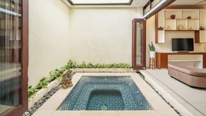 A modern bathroom with a freestanding bathtub, a shower area, and a built-in seating area with a television. - The Seven Residence (Kerobokan)