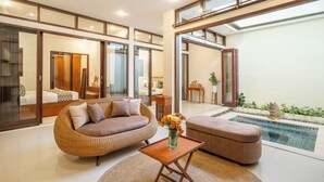 A modern living room with a sofa, ottoman, and a small table with a vase. There is a pool in the background. - The Seven Residence (Kerobokan)