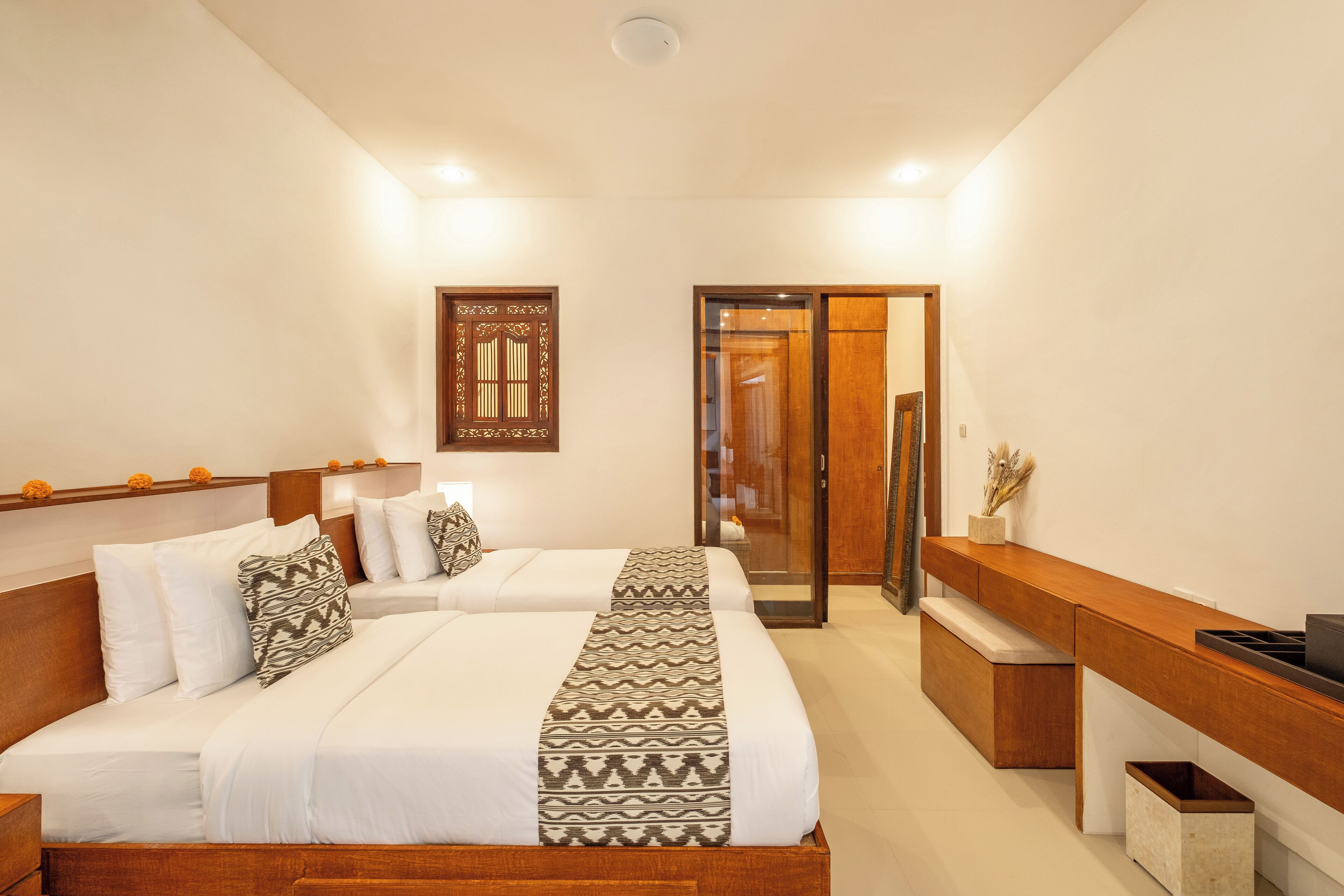 A hotel room with two beds, a wooden bench, a desk, and a sliding door.
