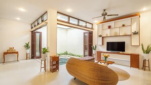 A spacious living room with a large TV, wicker furniture, and a balcony with a pool. - The Seven Residence (Kerobokan)