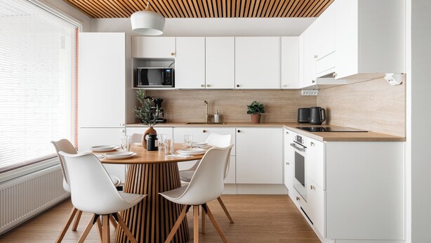 Een moderne keuken met witte kastjes, een houten plafond en een eethoek met witte stoelen en een houten tafel.