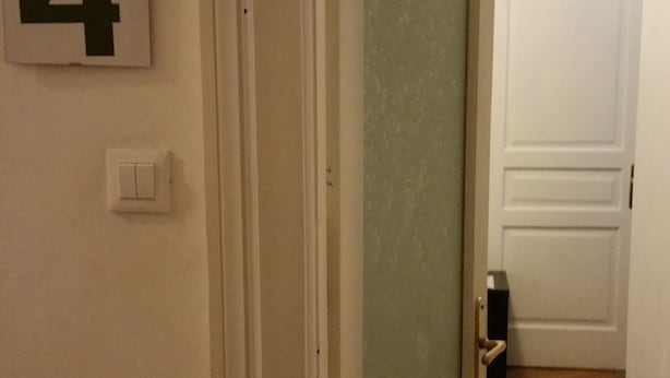 A hallway with a door leading to a room, a number '4' sign on the wall, and a light switch. - Affittacamere Guerrero Jr (Trieste)