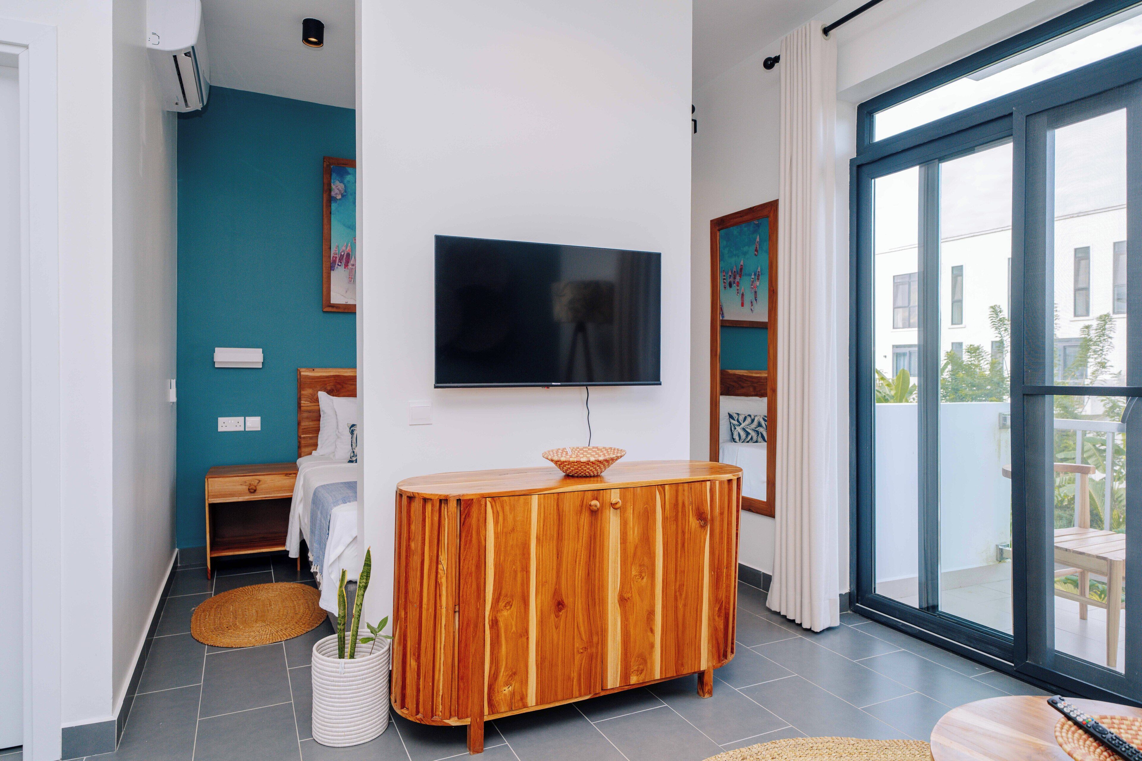 Un salon moderne avec un téléviseur fixé au mur, un meuble en bois et une grande porte-fenêtre coulissante donnant sur un espace extérieur.
