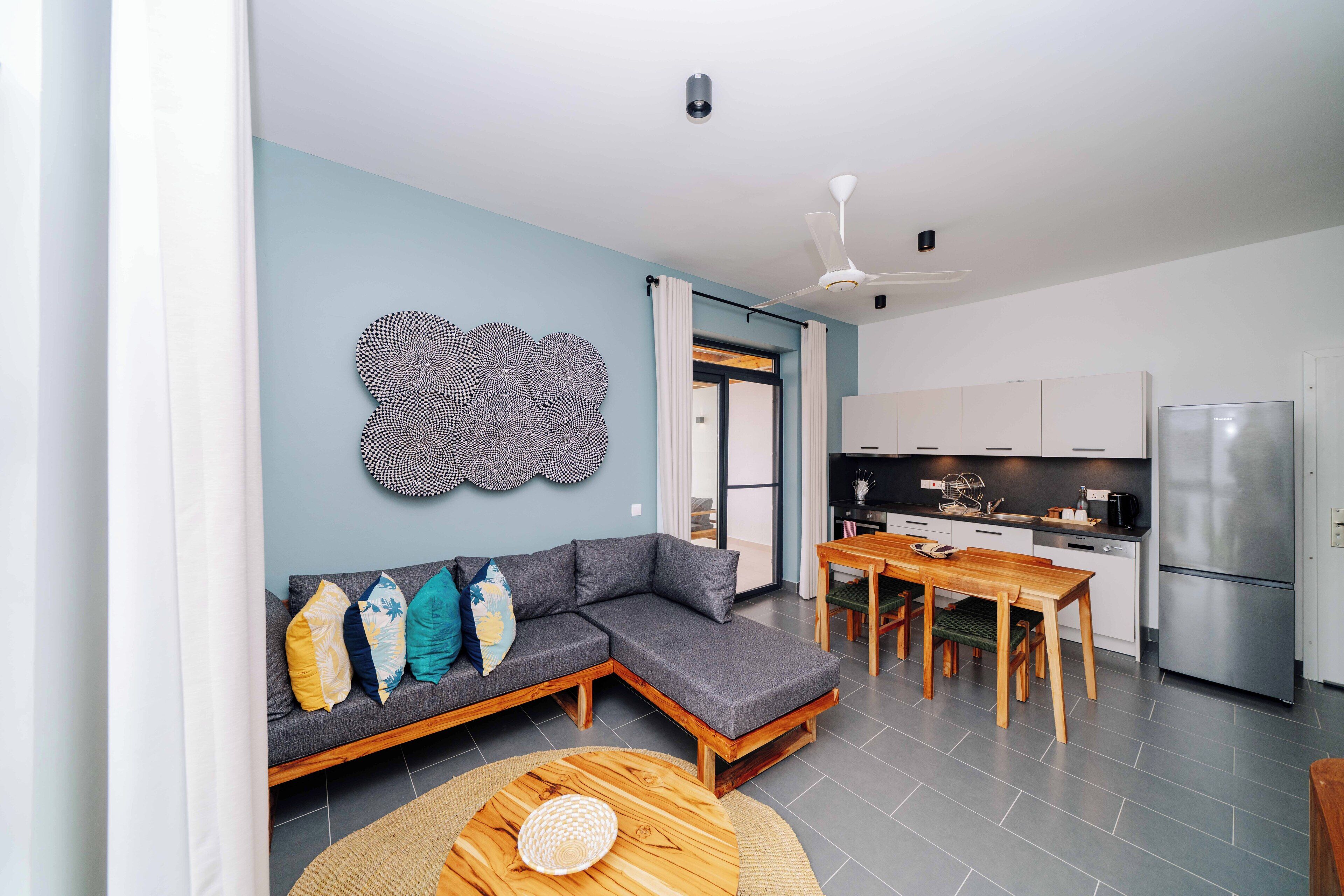 Una sala de estar moderna con un sofá seccional gris, una mesa de comedor de madera y una cocina con refrigerador de acero inoxidable.